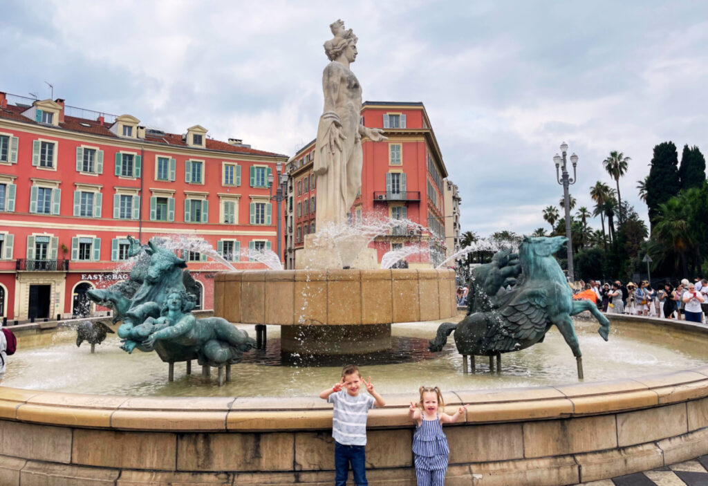 Kids standing in front of famous fountain in the middle of a square in Nice France