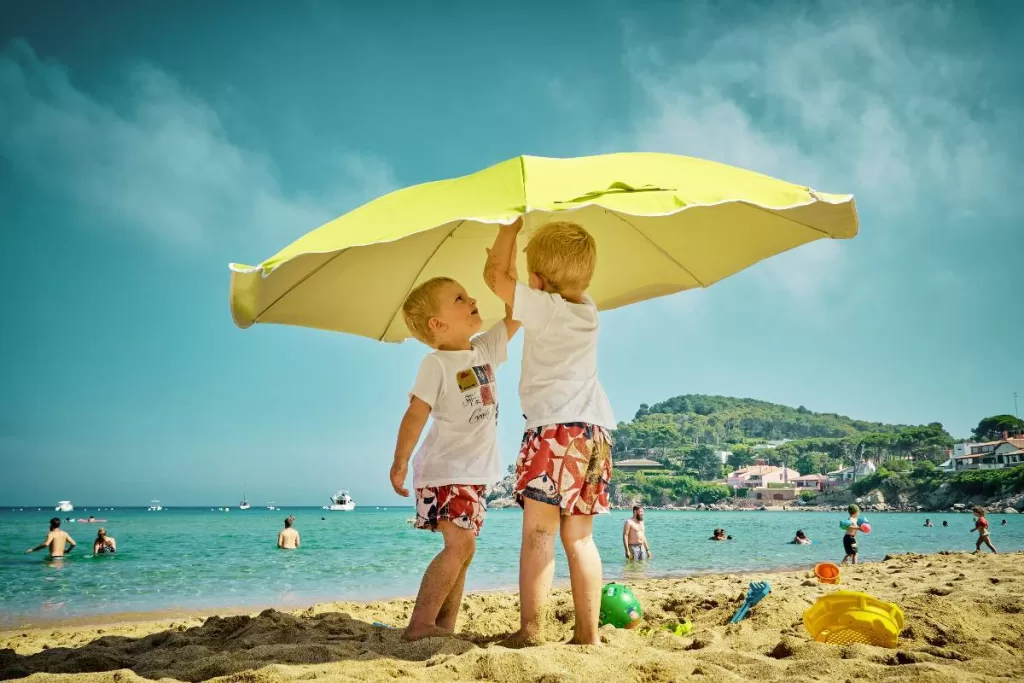 Two kids playing on beach under umbrella