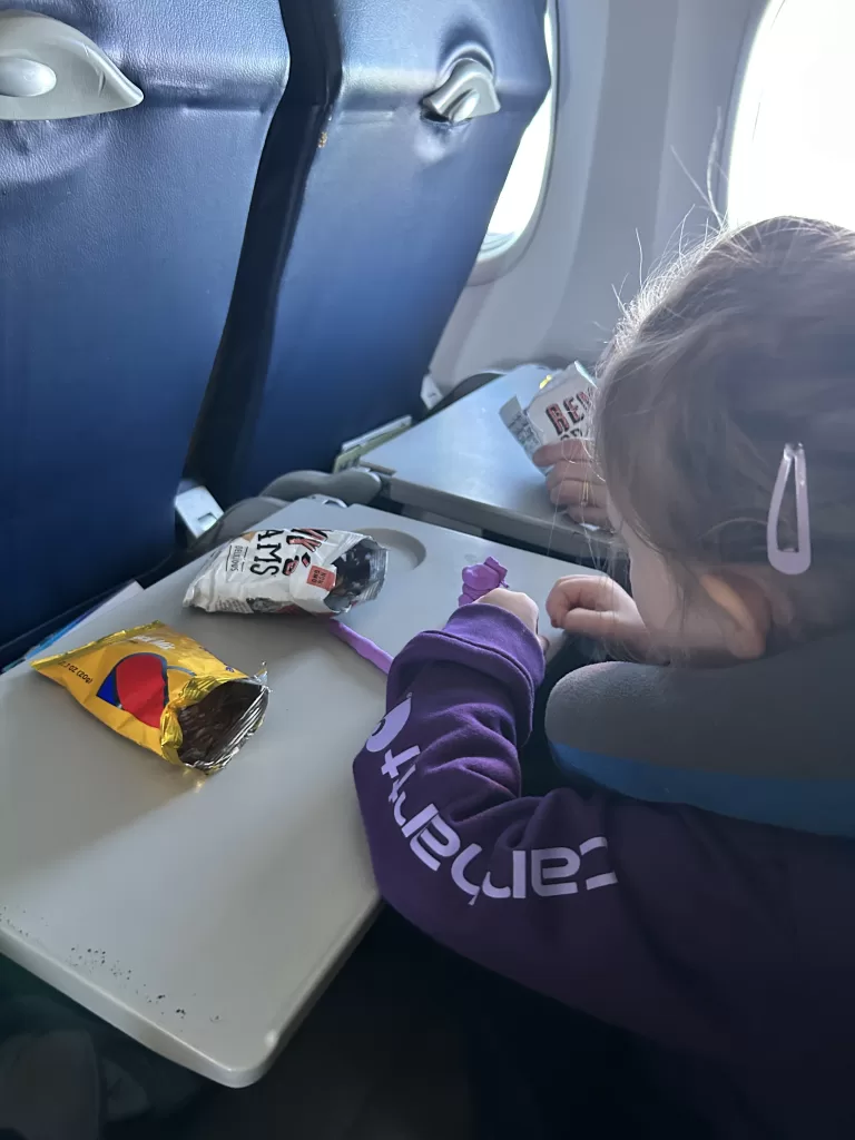 girl in purple coat eating snacks on an airplane.  Toddler airplane snacks