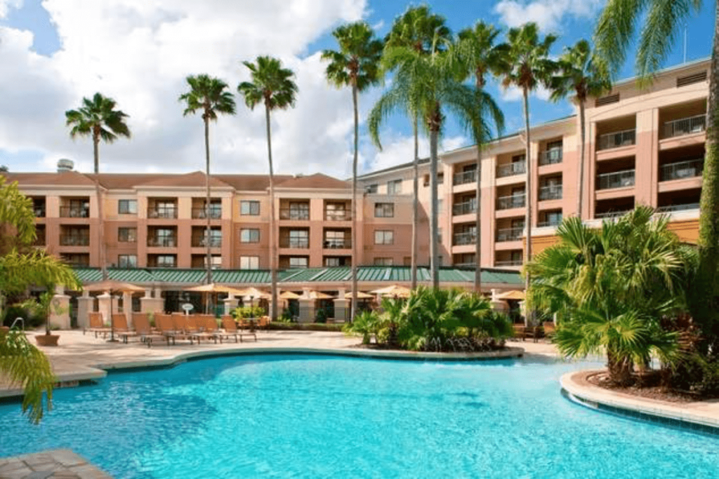 Hotel with palm trees.  Three story brown building with pool