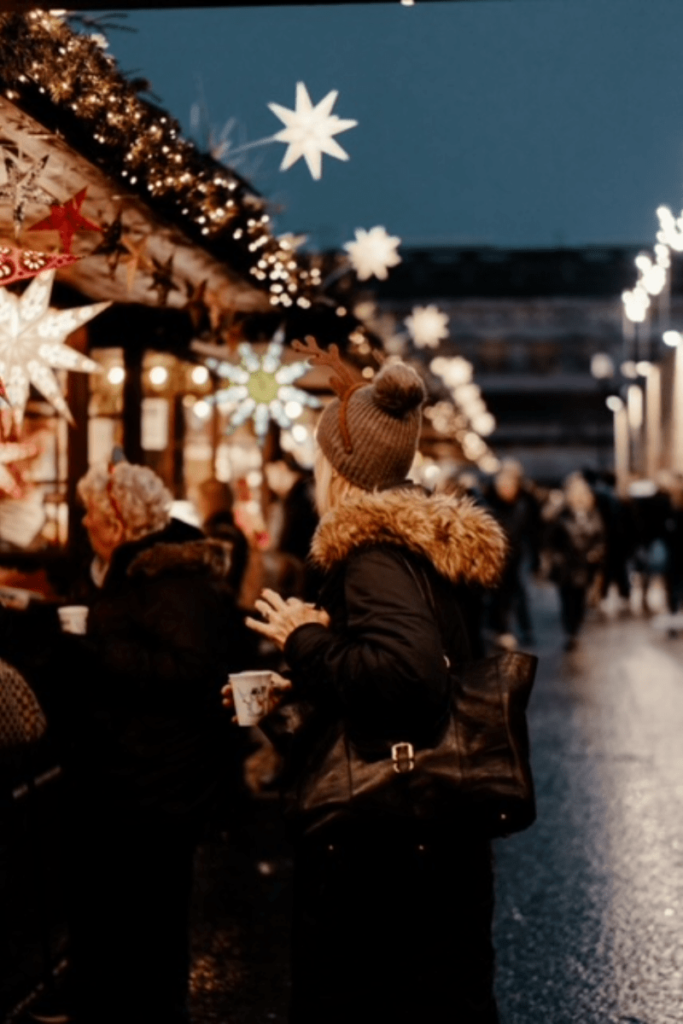 Christmas lights at a Christmas market.  Women with stocking cap on is shopping
