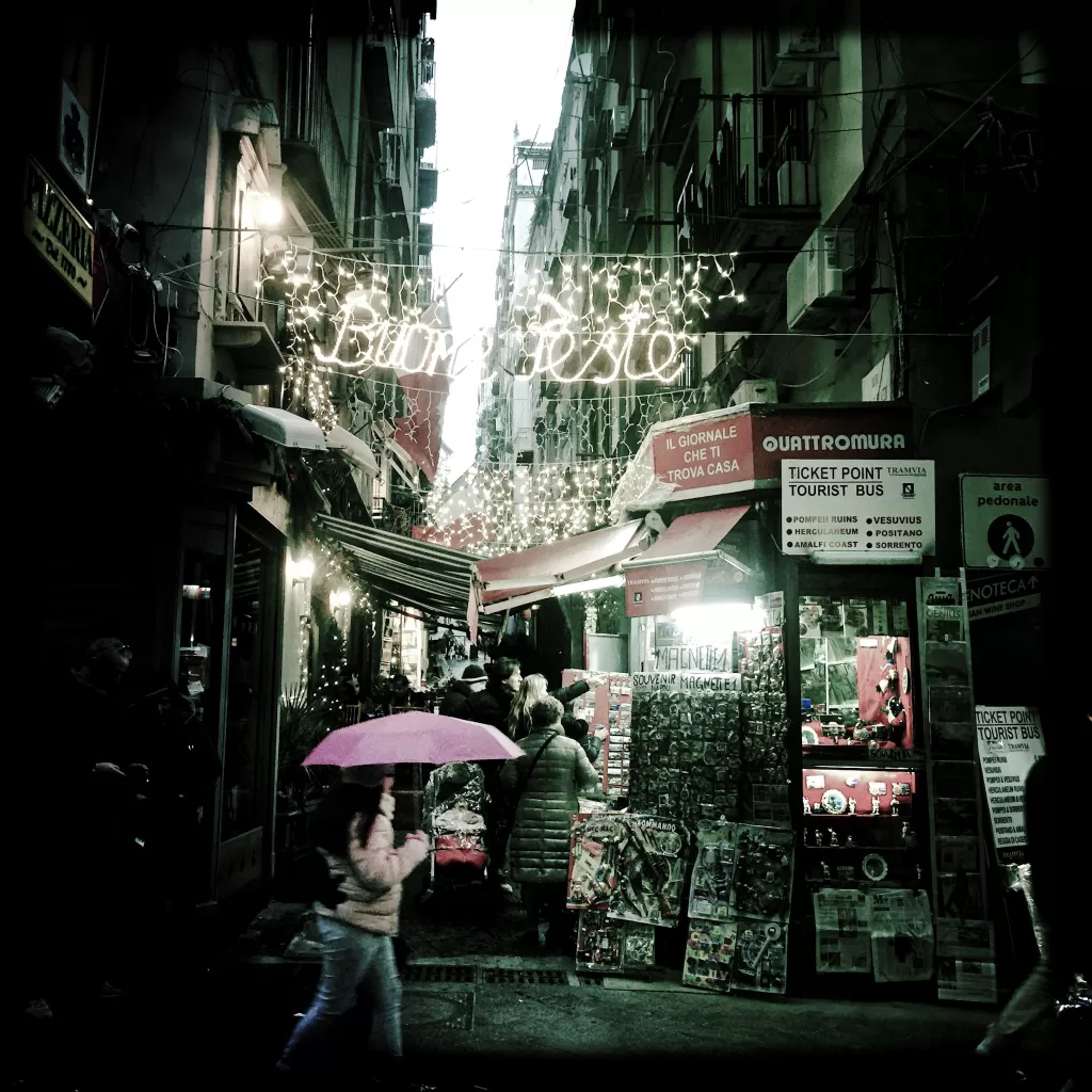 Naples with christmas lights between the buildings and a woman walking with a pink umbrella