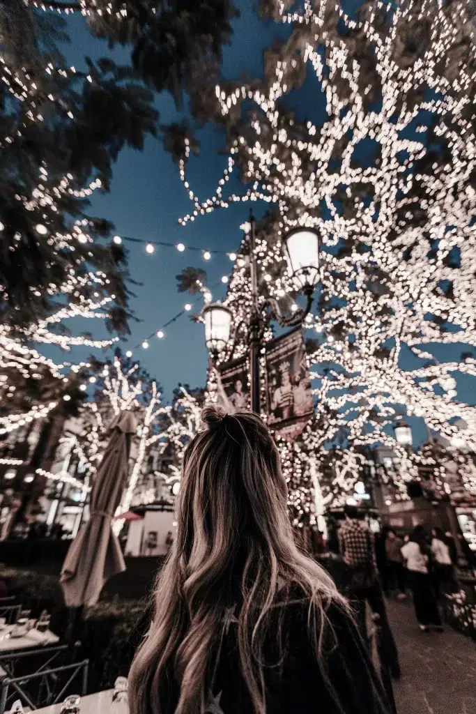 Christmas lights in trees with woman looking up at the twinkles
