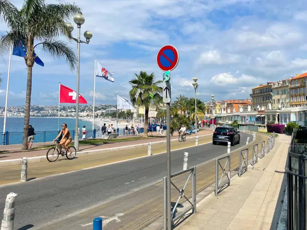 Promenade des Anglais in Nice.  Palm trees with flags and bike riders by the beach