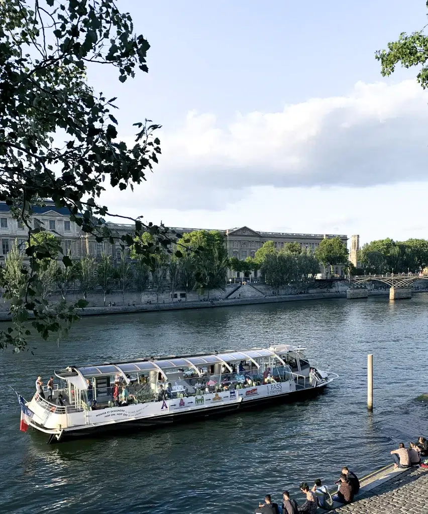 River boat on the Seine river in Paris with people looking on from the bank