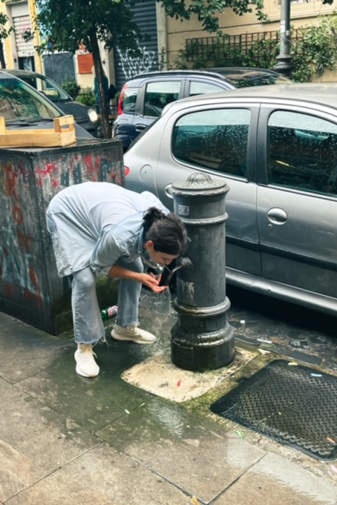 Woman drinking out of a public water fountain in Rome