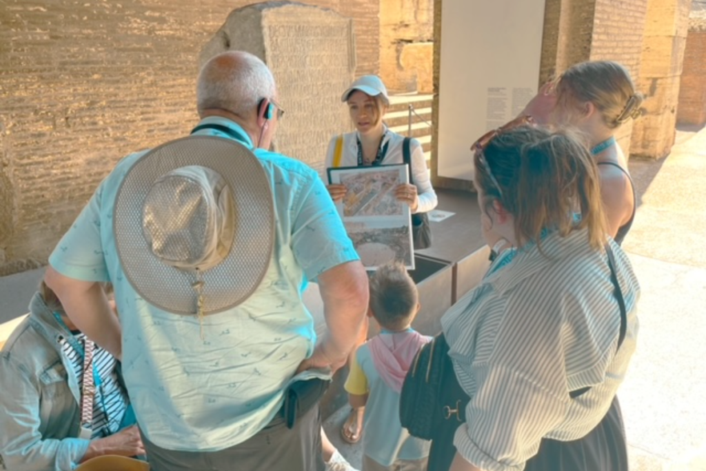 Group of tourists at the Colosseum looking at tour guide.  Man is wearing a large hat.  Dress Code Colosseum