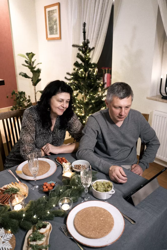 Two people sitting around a holiday table skyping with family.  Christmas trees in the background