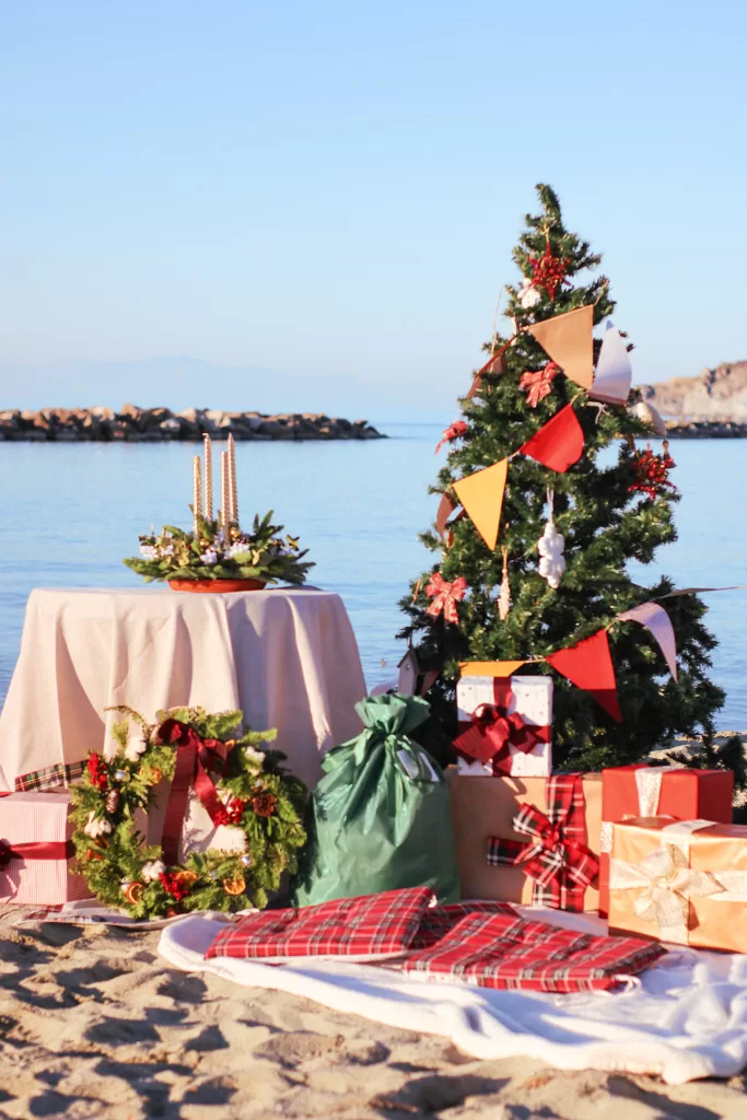 Christmas Tree decorated with red and yellow flags sitting on a beach.