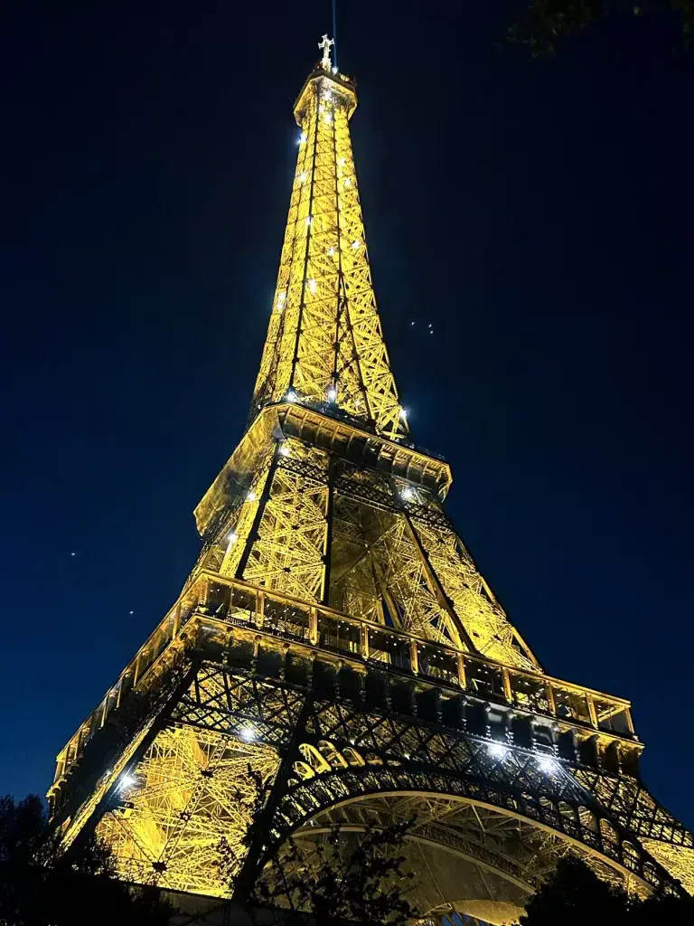 Eiffel tower lit up at night with yellow lights.  Madrid vs. Paris