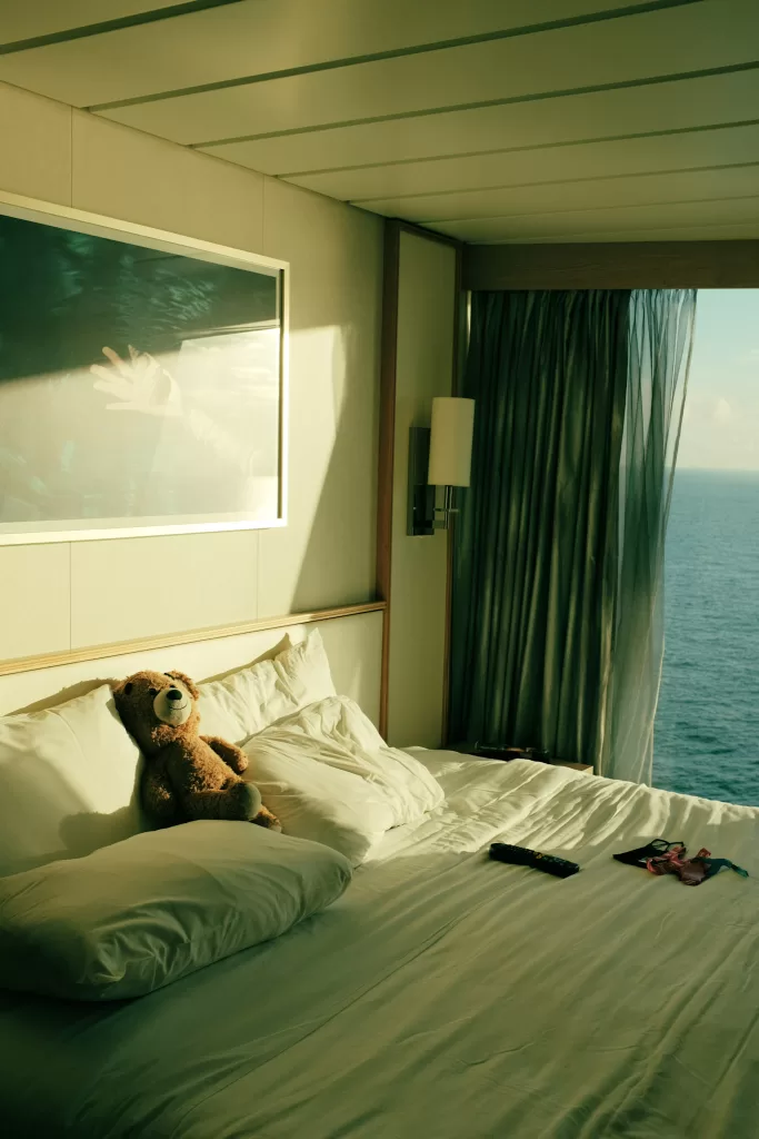 Teddy bear sitting on a white bed in a cruise cabing.  How to sleep on a cruise