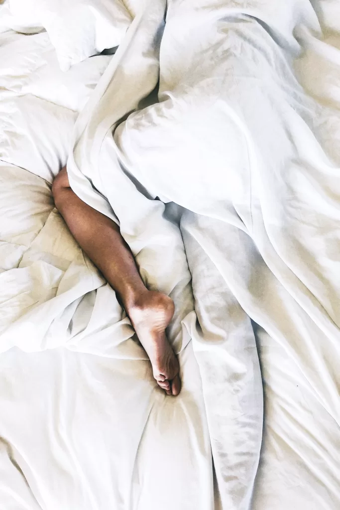 white sheets in a bed with a person laying in it. 