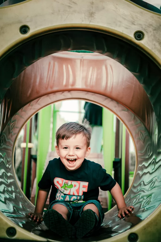 Small child smiling in a tunnel at an indoor playground.  Airport playgrounds