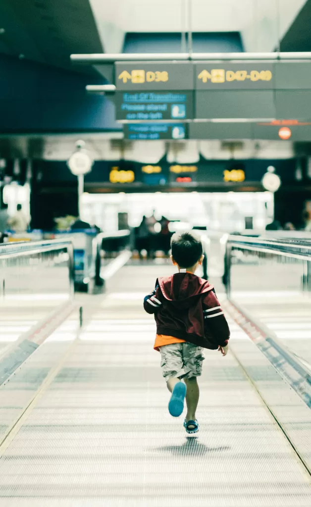 Small child with red jacket running down airport terminal 