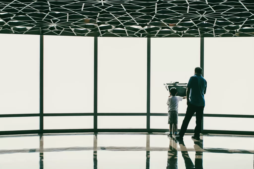 Dad and small son at an airport terminal looking out at the runway through large windows