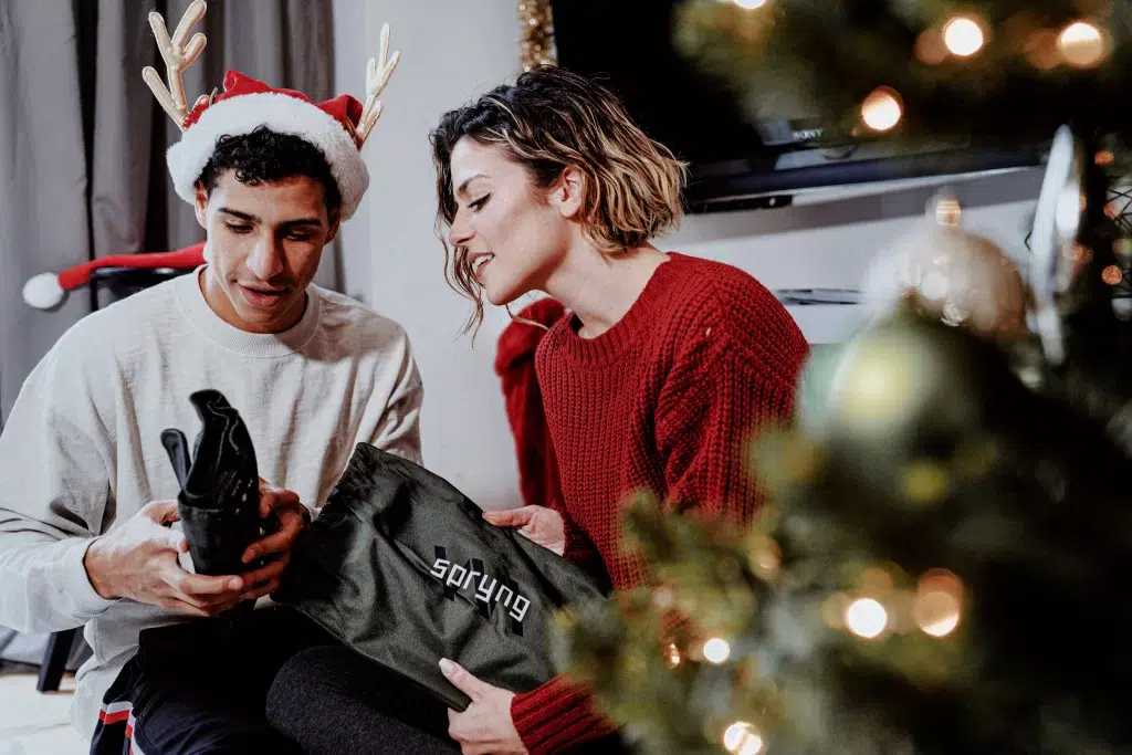 Teenage boy in christmas santa hat with women in red sweater on Christmas day with christmas tree in forground