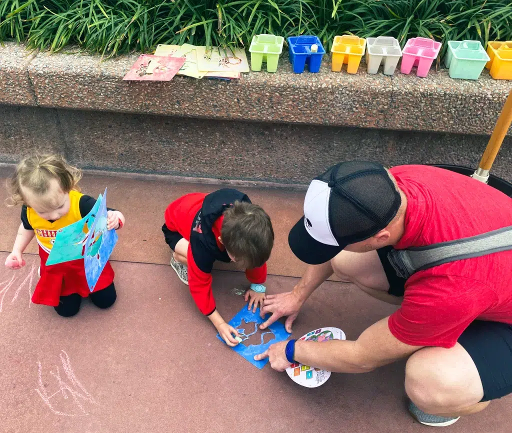 Two small kids drawing with chalk wtih their dad.  Epcot's festival of the arts with kids