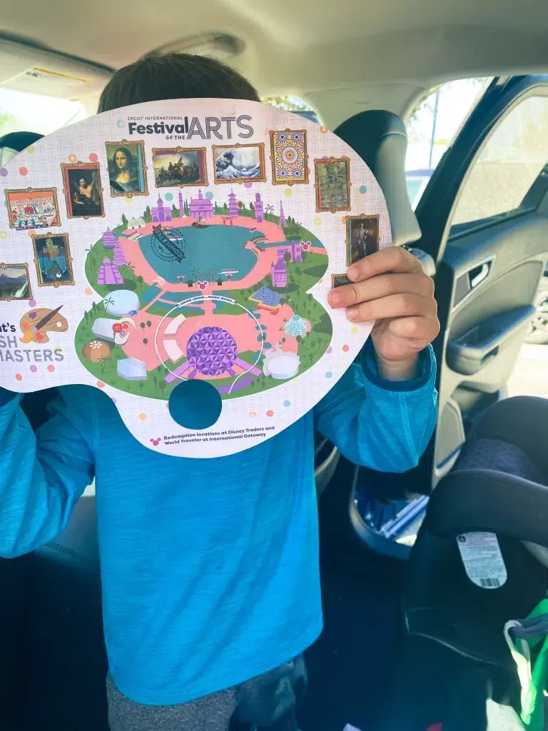 Small child holding up a paper scavenger hunt from Disney's Epcot