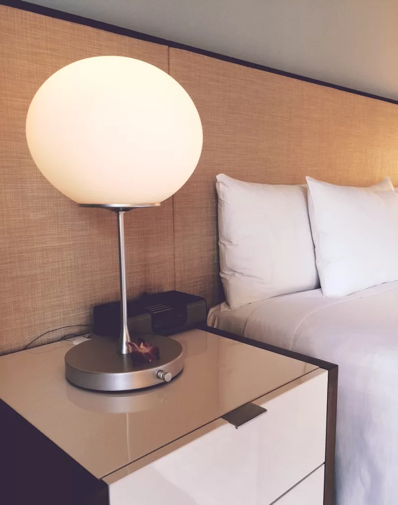 Hotel Room with bed. Bed has white sheets. SIde table has round spherical lamp on it.,