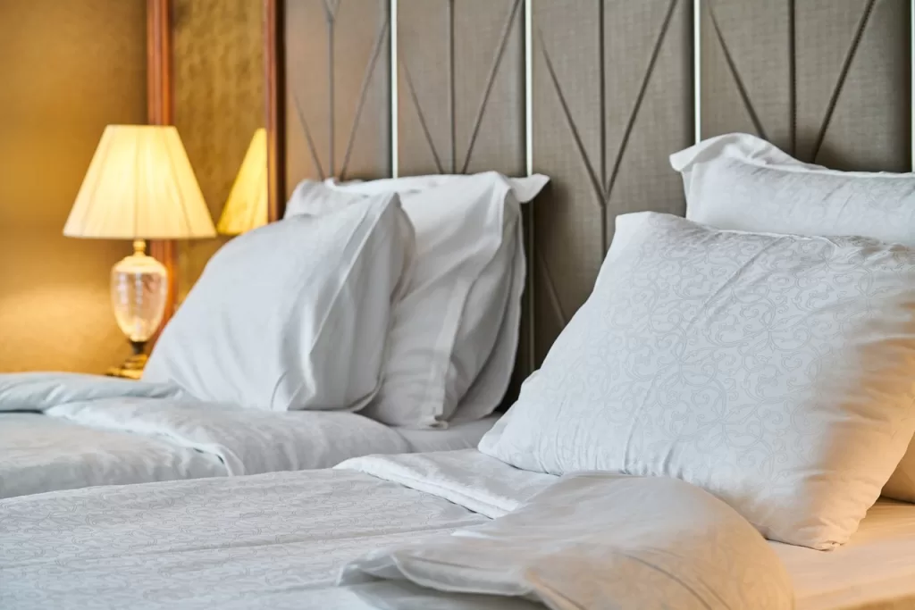 Two hotel beds with white sheets and lamp in background. Extra Bed Hotel