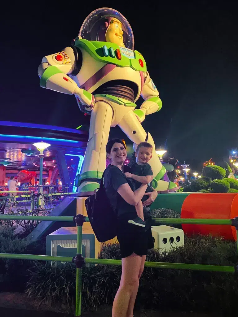 Mom holding a son in front of a giant buzz lightyear statue