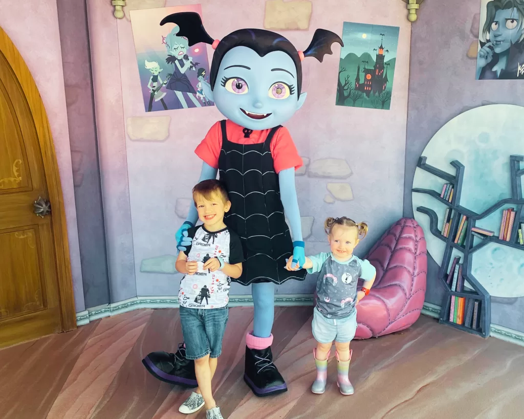 a boy and girl standing next to large character dressed as vampirina at disney world
