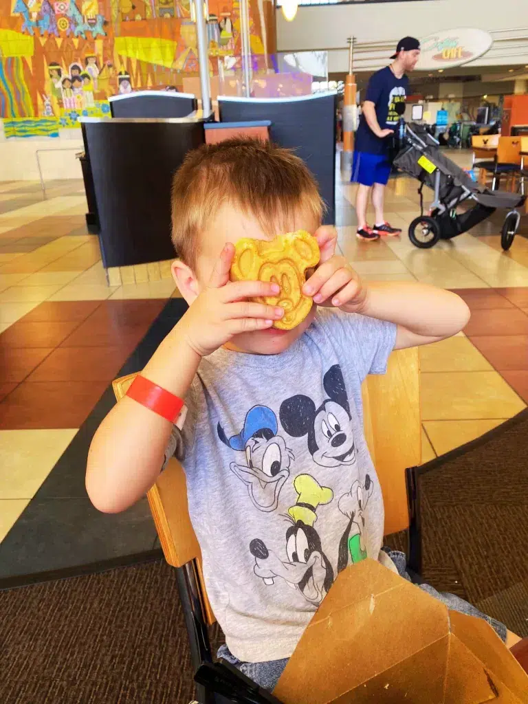Small boy holding up a mickey mouse shaped waffle over his face. 