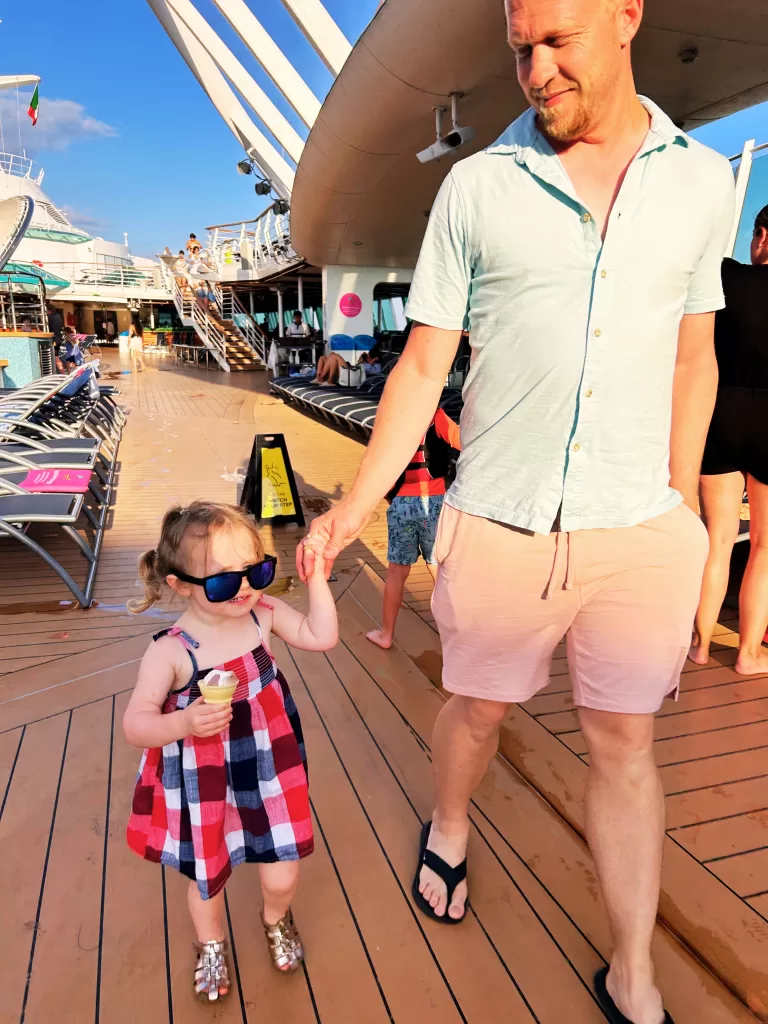 small girl in blue and red dress eating an ice cream cone and holding her dad's hand