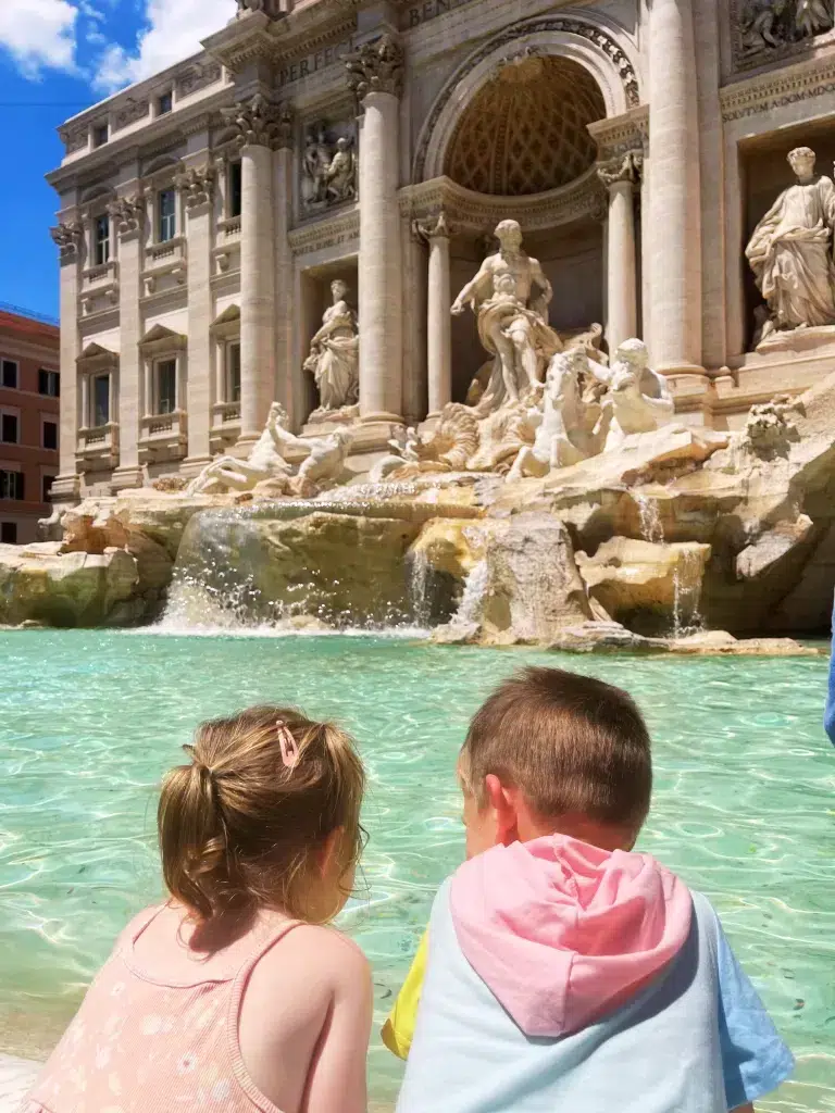 Two small children looking on to the Trevi fountain.