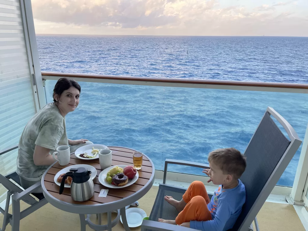 Mother and son sitting out on cruise ship balcony enjoying room service on small round table.