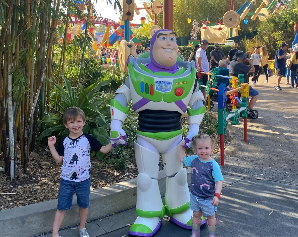 Two children dressed in summer clothes standing next to Buzz Lightyear at Disney World