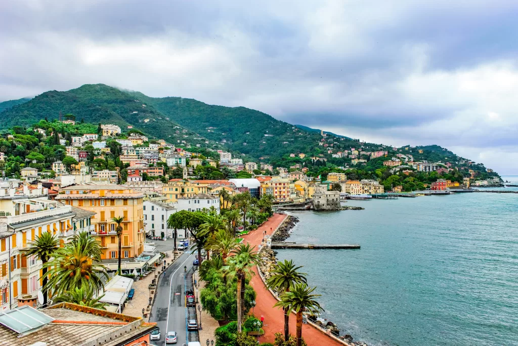 Large coastline in rapallo, italy. palm trees line boardwalk and coloful buildings overlook the ocean.