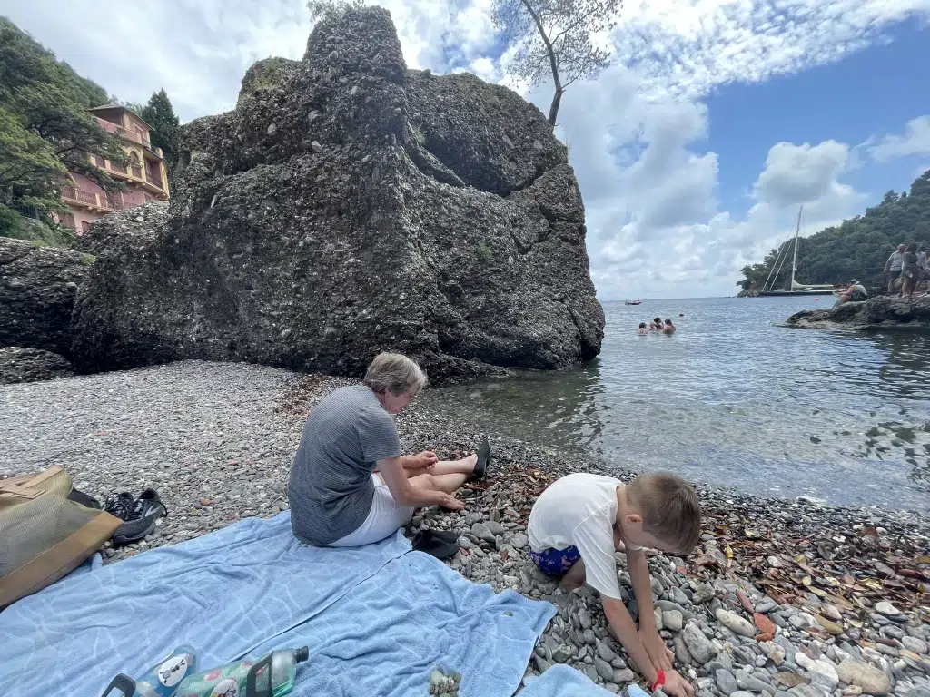 Grandmother and young boy play on rocky beach in portofino italy.