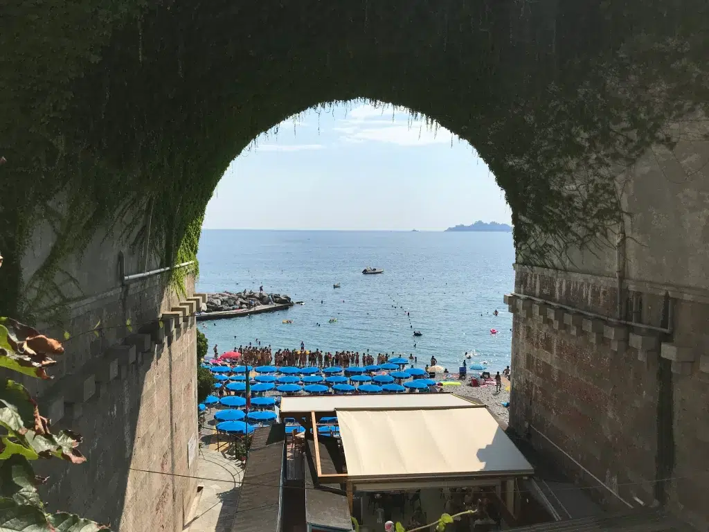 zoagli beach in italy.  Blue umbrellas in the distance with med sea.  View is taken through tunnel overlooking beach, 