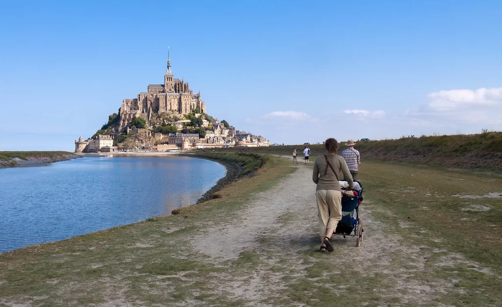 mont st michele in the distance with mother and baby stroller walking towards the fortress