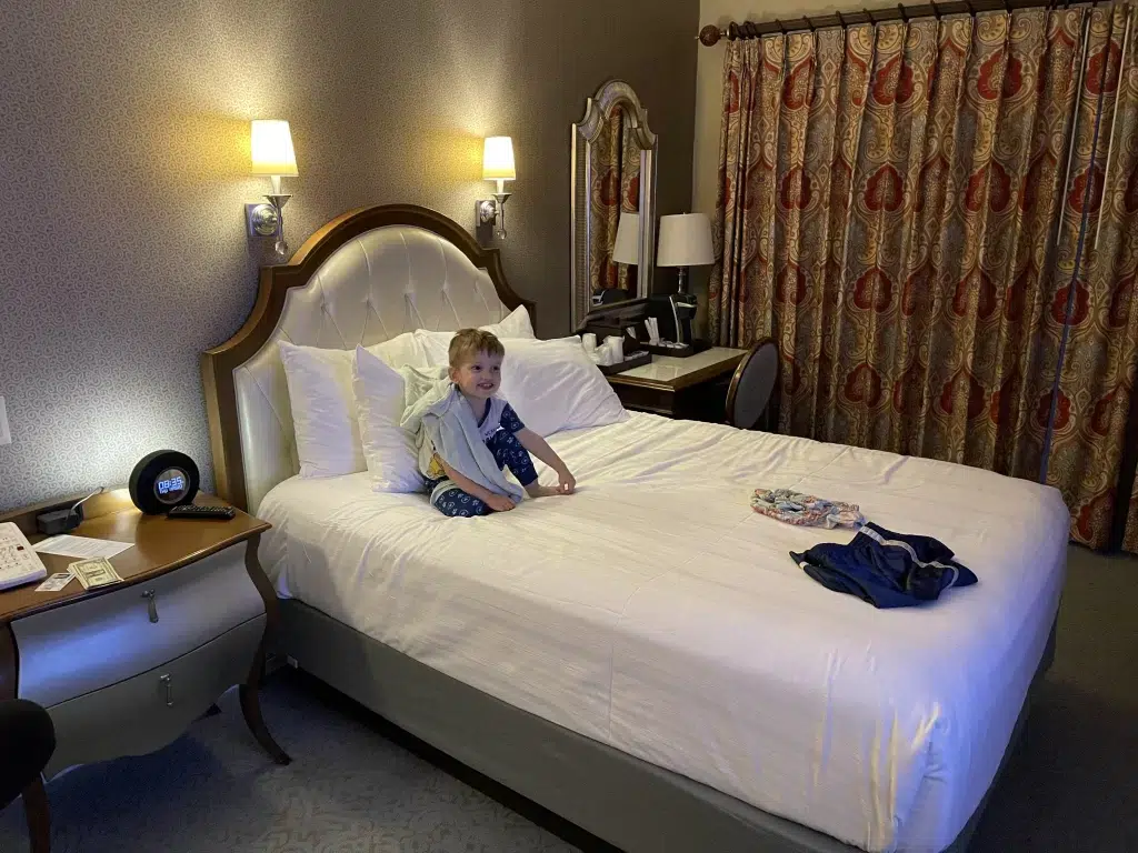 Young boy sitting on bed in the grand floridian hotel in Disney World