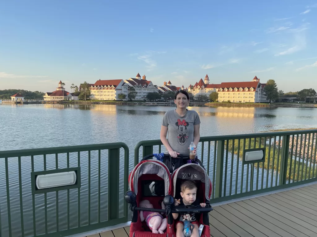 Mom in a mickey mouse shirt standing in front of the grand floridian resort with stroller and two kids.  Grand Floridian with kids