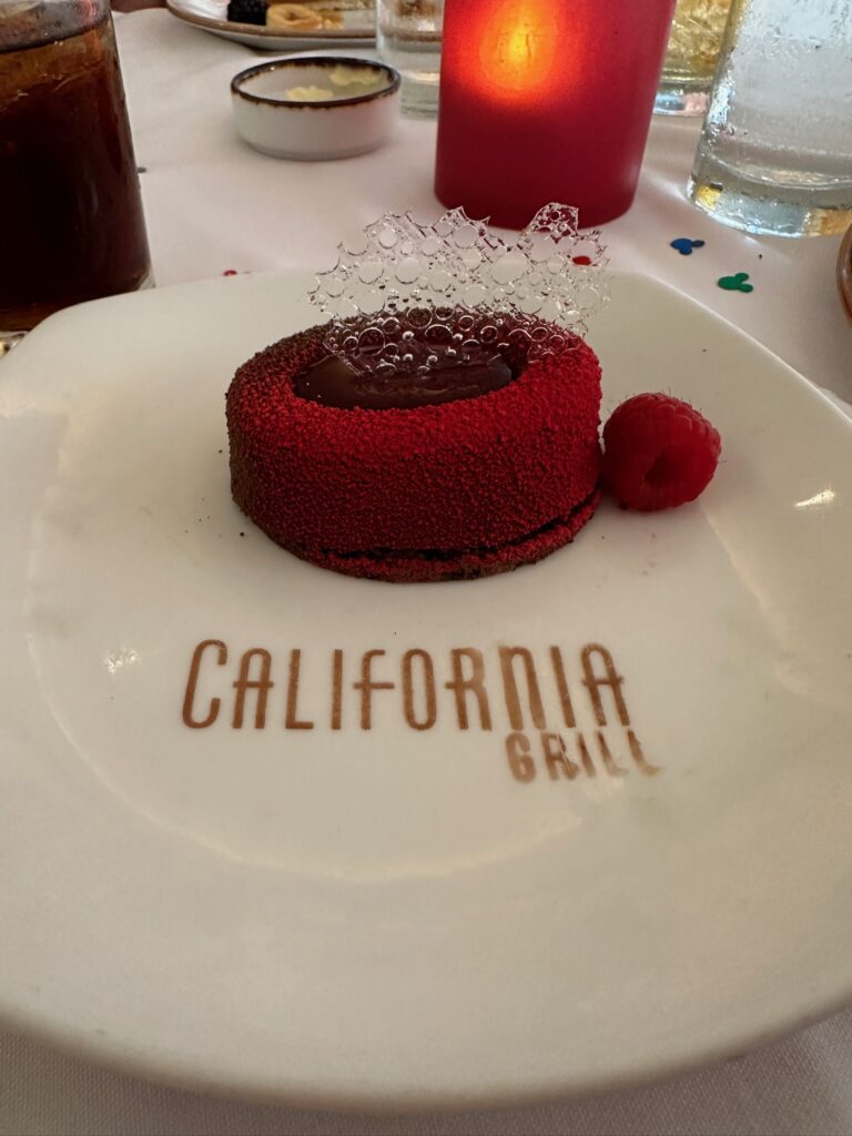 Beautiful red dessert topped with sugar art on a plate that says "california grill"